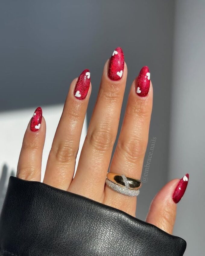 Ongles rouges scintillants avec des motifs de cœurs blancs