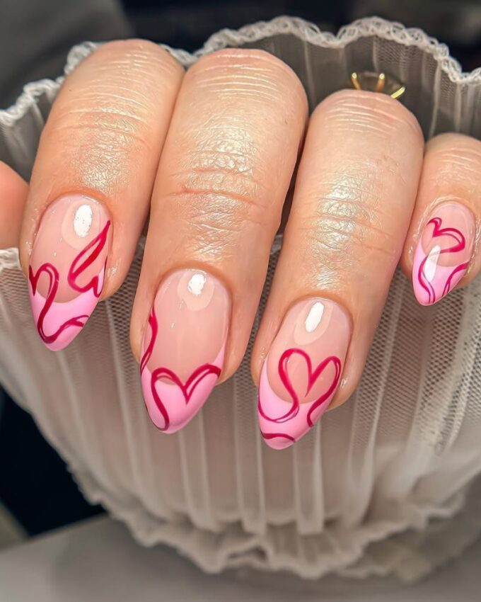 Manucure rose French avec des cœurs rouges en nail art.